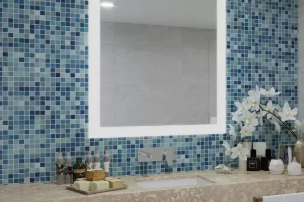 Frosted light-framed mirror installed in a blue mosaic tiled wall with white flowers.