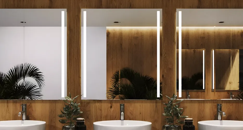 Custom lighted mirror with marble frame in modern bathroom featuring marble walls, gold fixtures, and elegant lighting.