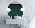 A thumb of circular-backlit mirror with chianti lamp on a white marble wall above a cabinet sink.