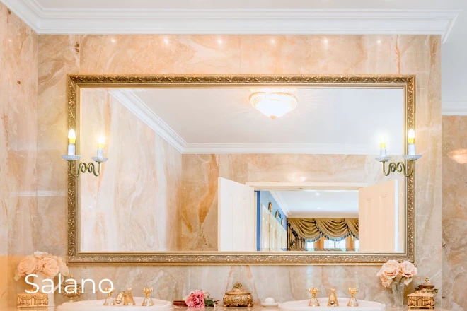 Elegant golden-framed mirror with a decorative salano lamp set on the wall above a basin.