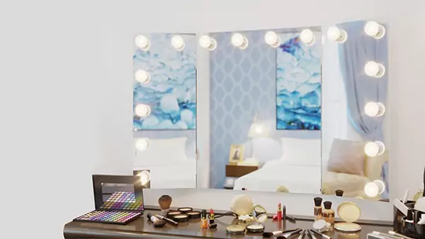 Thumb of trifold Hollywood mirror is mounted on the wall above a table of makeup essentials.