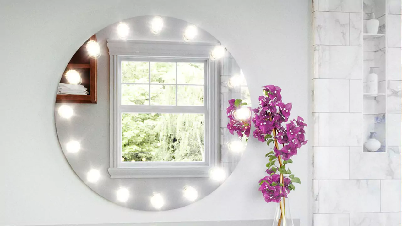 A round Hollywood mirror is set on a white wall with a purple-pink Bougainvillea flower.