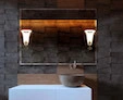 A compact piloni lamp in a custom mirror is set on the wall above a brown stone sink bowl.