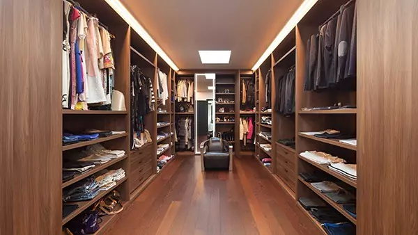 A compact of walk-in wooden closet with an illuminated mirror and a small lounge chair.